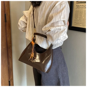 Détail du sac demi-lune en cuir marron foncé avec pompon en perles et logo gravé