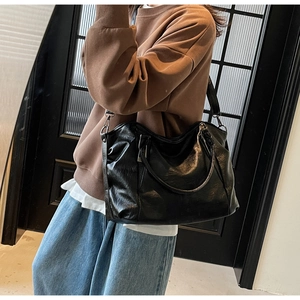 Detail of a large black soft leather tote bag worn by a model in casual streetwear style