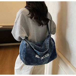 Detail of blue denim shoulder bag featuring a white REPLACED print and wide strap