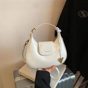 Macro detail of creamy white crescent bag featuring a gold heart charm on silver case