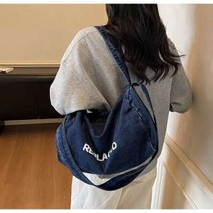 Model wearing a large navy denim shoulder bag with white REPLACED text lettering