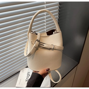 Close-up of litchi pattern leather bucket bag in cream white with adjustable metal buckle strap