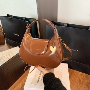 Detail of a brown polished leather hobo bag with a gold heart pendant and strap