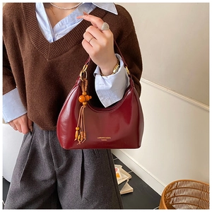 Détail du sac demi-lune bordeaux en cuir brillant avec pendentif en perles de bois
