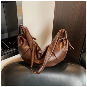 Detail view of brown pleated crescent underarm bag with knotted strap and soft leather texture
