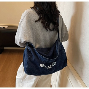 Detail of the large blue denim tote bag with white REPLACED embroidery shown on model