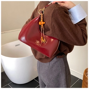 Détail du sac hobo en cuir bordeaux avec boucles dorées et breloque perlée élégante
