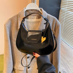 Detail of black patent hobo bag with gold heart pendant and woven handle knot