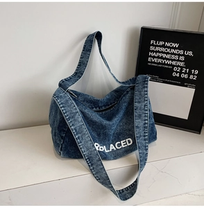 Detail of vintage blue denim crescent shoulder bag featuring bold REPLACED printed text