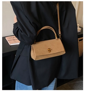 Détail du sac baguette mat kaki avec boucle dorée sur un blazer noir en mode porté
