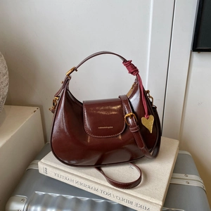 Detail of burgundy hobo bag with gold heart charm and braided strap on creative background