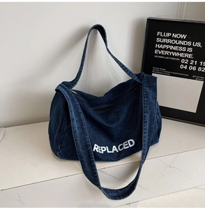 Detail of blue denim tote bag with white REPLACED text and secure black zipper closure