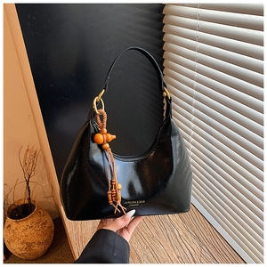 Gros plan d'un sac hobo noir avec des anneaux dorés et un pompon en perles de bois