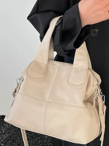 Minimalist beige tote bag in lychee leather texture with crossbody strap on black blazer