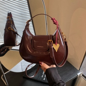 Detailed view of glossy dark purple crescent bag with gold heart pendant and woven knot detail