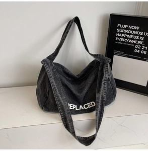 Detail of grey washed denim tote bag featuring white REPLACED lettering and hobo style