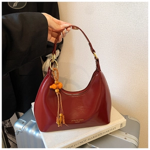 Détail du sac hobo en cuir bordeaux avec boucles dorées et pampille en perles de bois