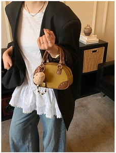 Detail of a vintage olive green bowling bag with white plush ball charm and metal rivets
