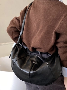 Minimalist black pleated hobo bag with retro half-moon design shown on model shoulder