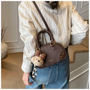 Brown leather bowling bag featuring plush bear charm shown on a crossbody model