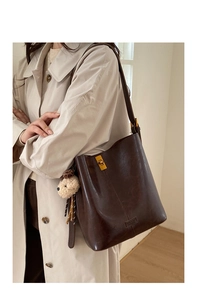 Detail view of a vintage brown bucket bag with gold twist lock and plush bear charm