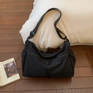 Detail view of black canvas shoulder bag with dual zippers and adjustable strap on wood floor
