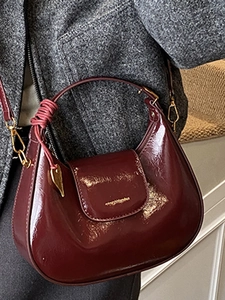 Glossy burgundy patent leather crescent bag with gold heart charm and knotted strap