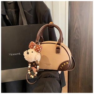 Detailed close-up of beige bowling bag with gold studs and cute plush bear charm