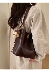 Deep brown bucket bag with a plush bear charm and metallic buckle shown on a model