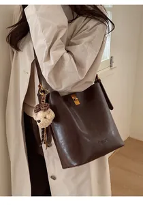 Detail of vintage brown bucket bag featuring a gold square lock and plush bear charm