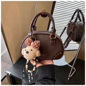 Detail of dark brown leather bowling bag with gold studs and cute teddy bear charm