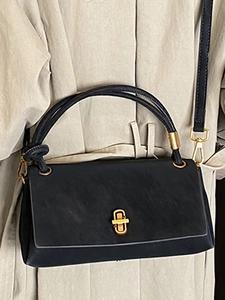 Sac bandoulière minimaliste noir mat avec boucle dorée sur un trench-coat beige