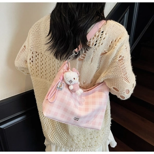 Détail d'un sac à bandoulière à carreaux roses avec un pendentif en peluche sur le côté