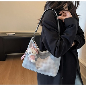 Gros plan d'un sac cabas gris quadrillé avec logo COIN CON et charm en peluche sur l'épaule