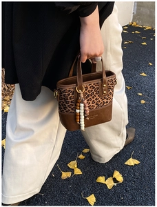 Detail of leopard print tote bag with wooden bead charm against autumn leaves