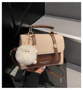 Close-up of retro saddle bag with contrast stitching and fuzzy plush ball charm