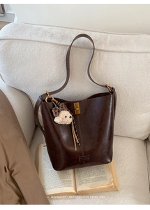 Detail of dark brown retro bucket bag with plush dog charm on a vintage book backdrop