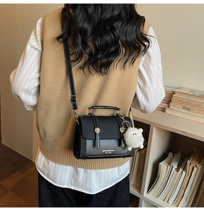 Close-up of black retro square crossbody bag with gold buckles and white sheep plush charm