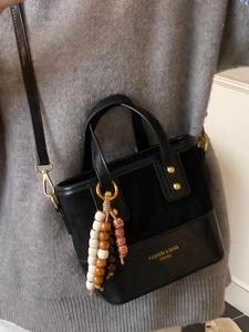 Minimalist black crossbody bag featuring suede patchwork and beaded tassel charm