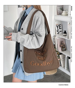 Close-up of brown tote bag featuring Never Say Goodbye yellow embroidery and curved design