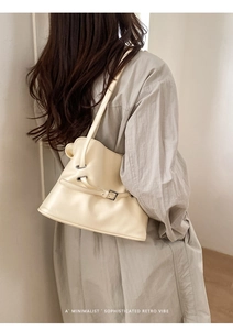 Détail d'un sac plissé crème avec boucle argentée porté à l'épaule par un mannequin