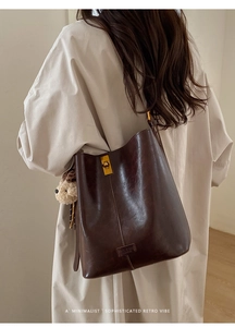 Detail of dark brown leather bucket bag with gold twist lock and a cute plush charm