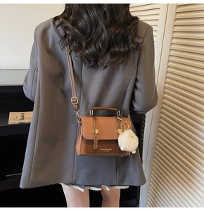 Detailed back view of a brown vintage crossbody bag with white fur ball charm accessory