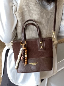 Chic brown suede and leather crossbody bag with vintage beaded pendant on a white shirt