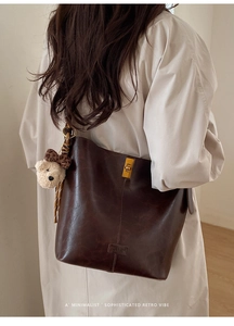 Detail of vintage dark brown leather bucket bag with gold clasp and teddy bear charm