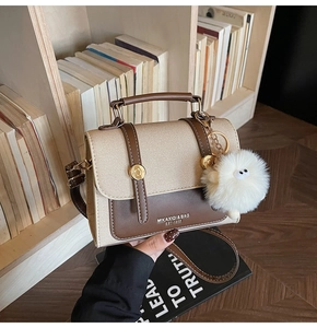 Detail view of a vintage crossbody bag with a plush monster charm on a wooden bookshelf
