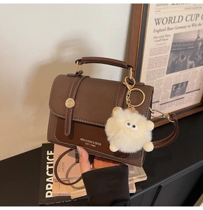 Detail of a brown textured vintage handbag with metal buckle and a plush ball charm