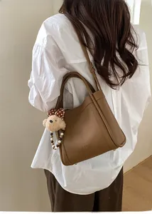 Detail view of brown lychee grain leather bucket bag with cute plush bear and bead charm