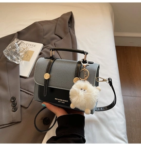 Detail of grey and black contrast leather bag with gold hardware and plush ball charm