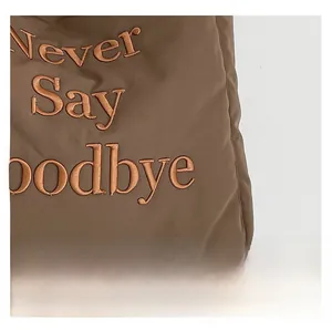 Detail of 3D embroidered text on brown nylon tote bag fabric with polished texture